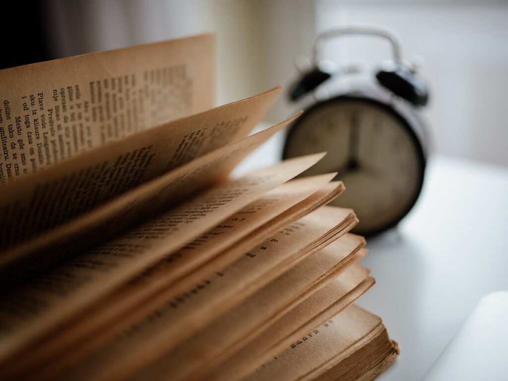 Old book pages flipping slowly next to a classic alarm clock on a table in a warm, inviting room